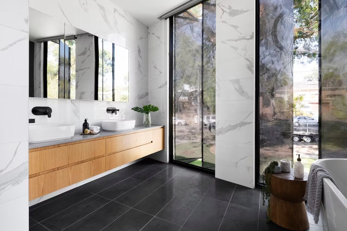 Ciepła, nowoczesna łazienka z wanną, brązowymi szafkami podumywalkowymi i lustrami p0owiększającymi wnętrze